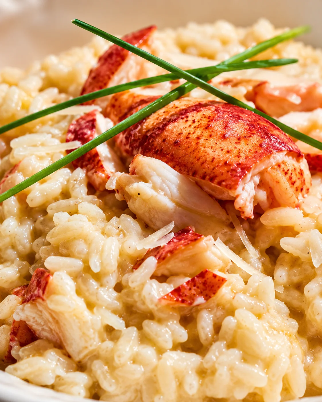 Creamy lobster risotto with lobster chunks and green chives on a plate.