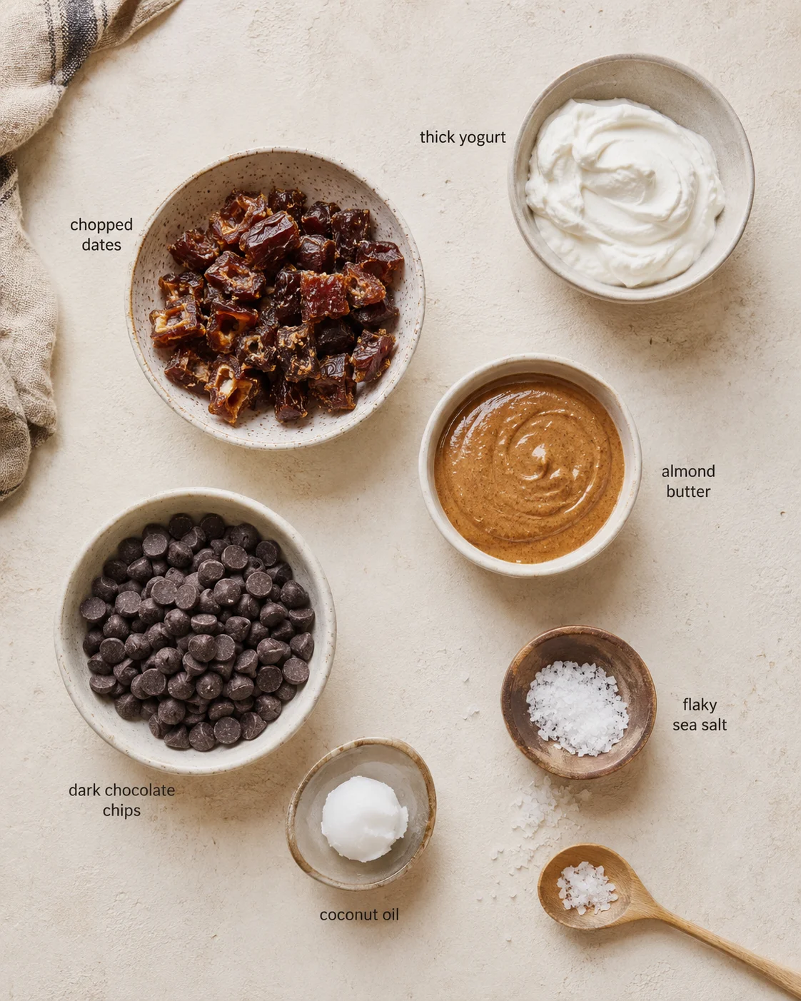 Top-down view of bowls with chopped dates, thick yogurt, almond butter, chocolate chips, coconut oil, and sea salt.