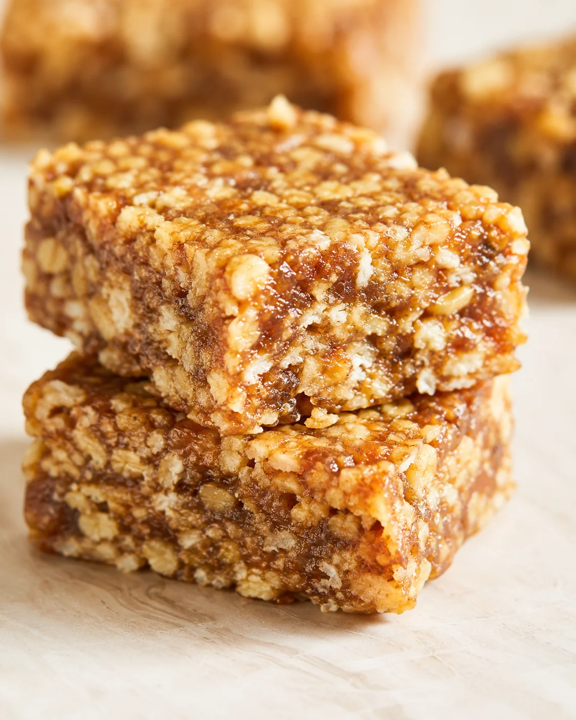 Close-up of stacked caramelized granola bars with oats and nuts on a light surface.