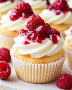 Close-up of a cupcake with white frosting and glossy raspberry topping on a wooden surface.