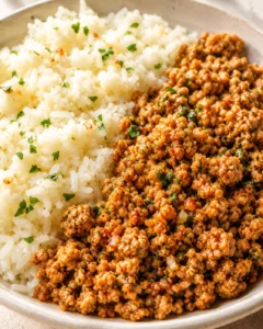 Close-up of fluffy white rice with ground beef and parsley on a warm ceramic plate.