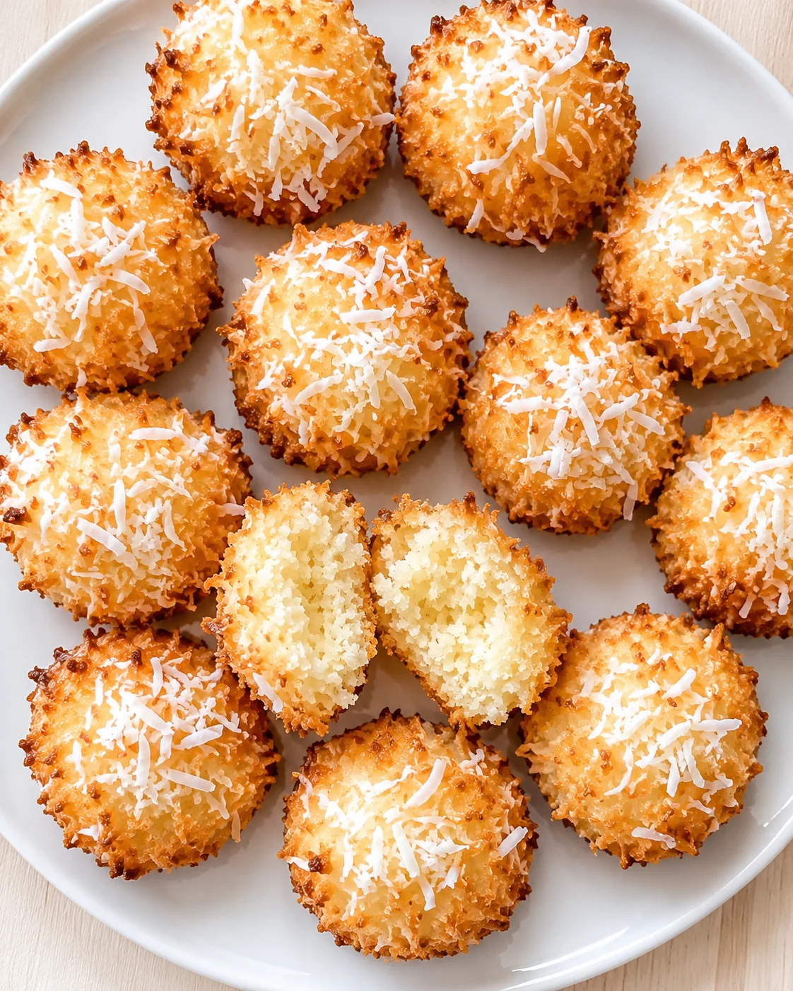 golden toasted coconut bites on a white plate, one broken open to show a soft interior