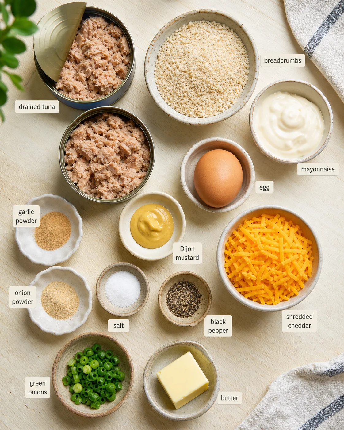 overhead shot of labeled tuna, breadcrumbs, mayo, egg, cheddar, and spices on a light wood surface