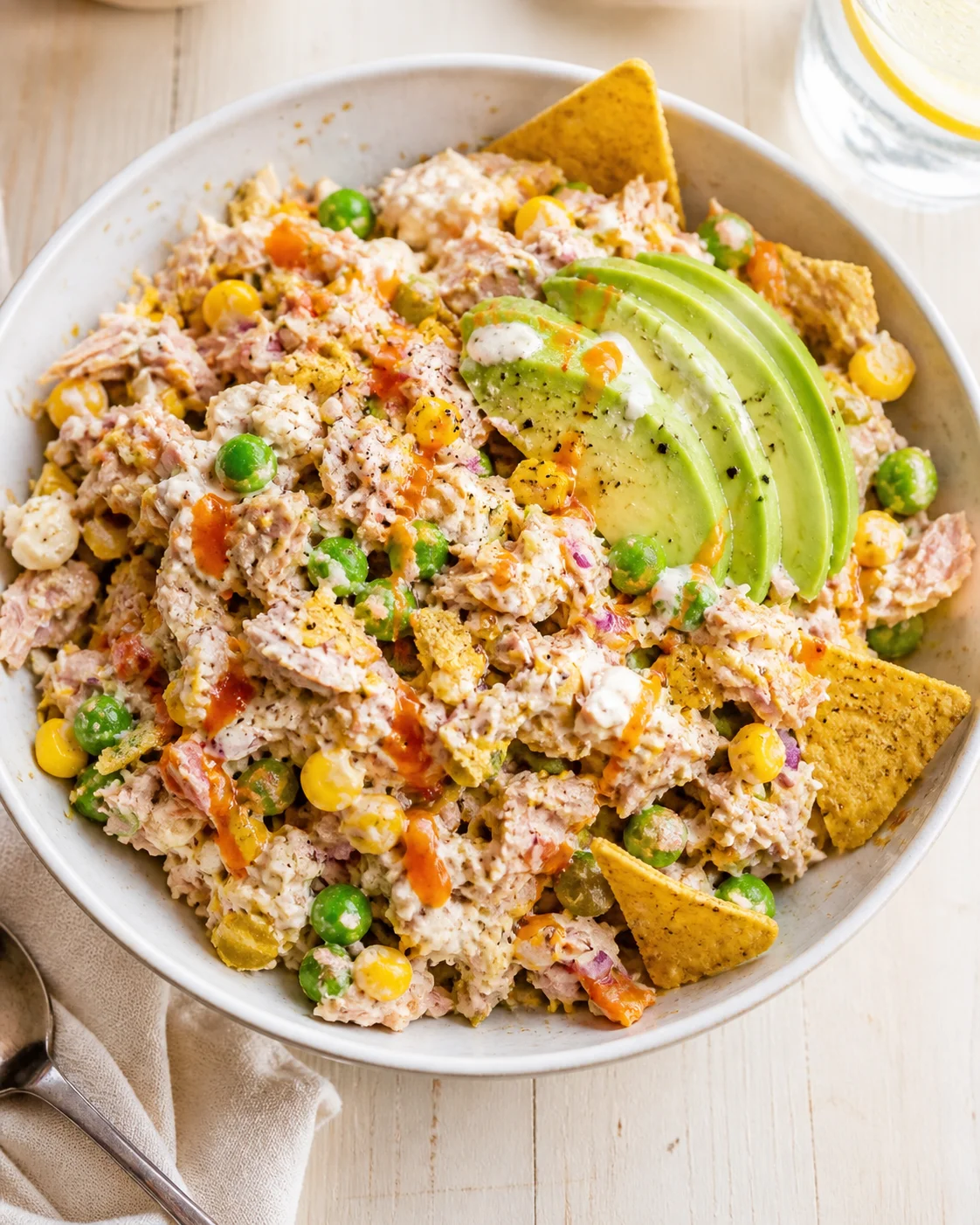 Creamy tuna salad with peas, corn, avocado slices and tortilla chips in a white bowl.