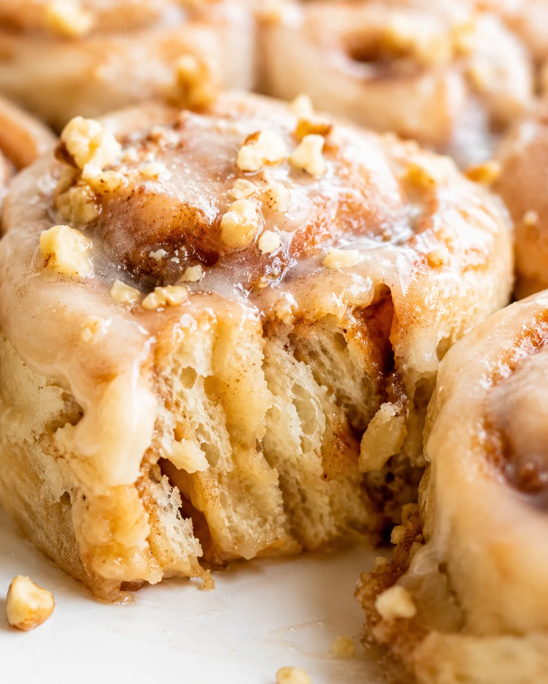 Close-up of glossy cinnamon rolls topped with walnut pieces, revealing soft, airy interiors.