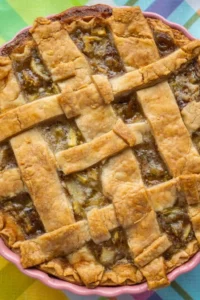 Golden lattice-crust fruit pie in a pink dish on a bright, colorful tablecloth.