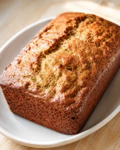 Golden-brown loaf bread with a cracked top, resting on a white oval plate.