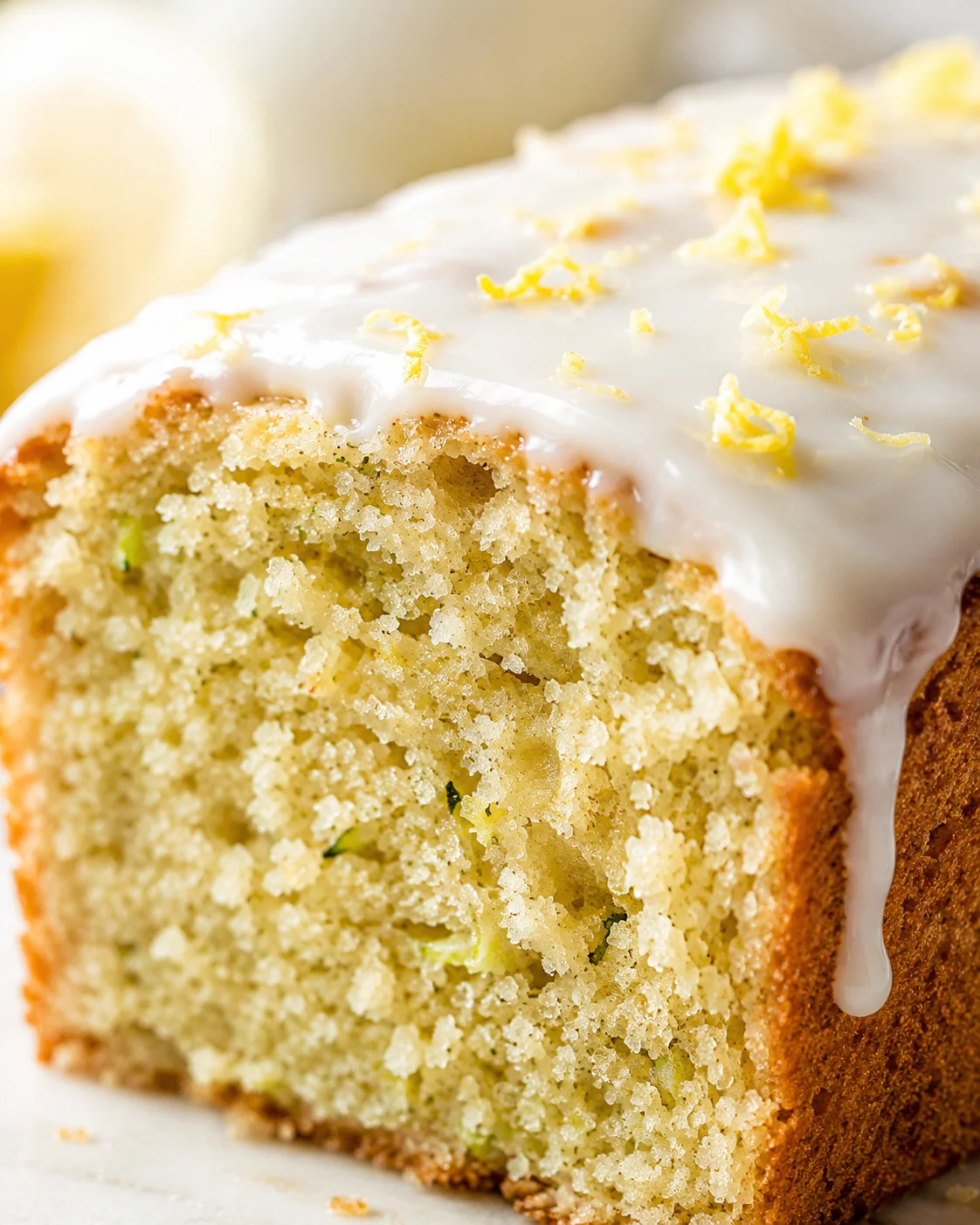 Close-up of lemon-glazed pound cake slice with moist crumb and lemon zest curls on top.