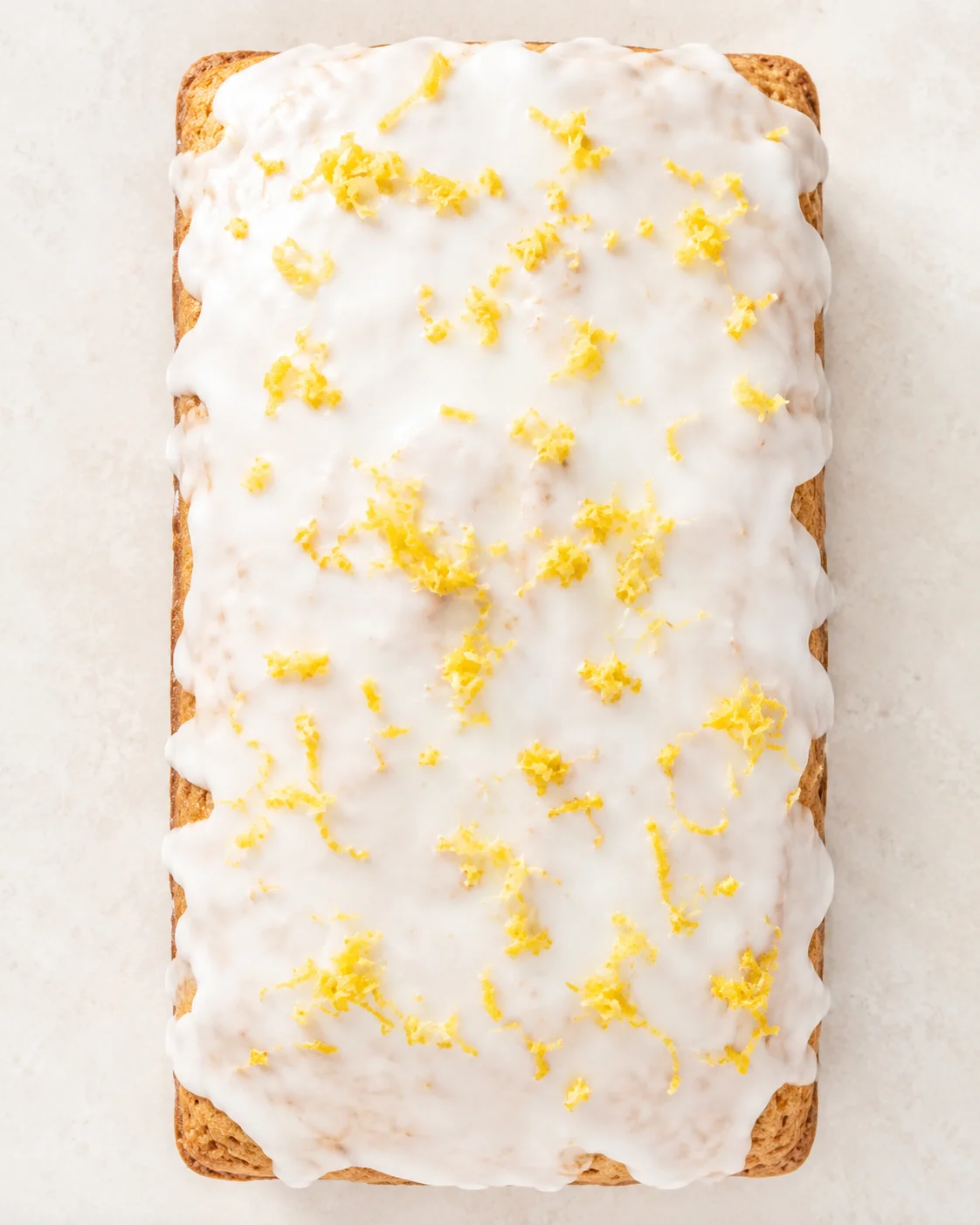 Rectangular lemon loaf cake with white glaze and bright lemon zest on top.
