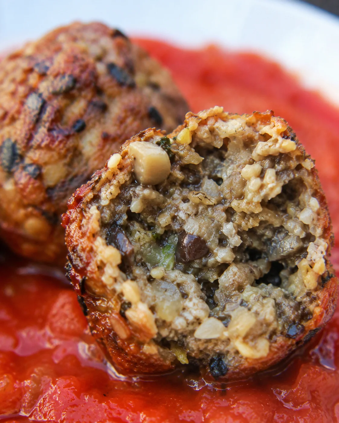 Eggplant Meatballs with Mushrooms and Garlic Close-up of savory vegetarian eggplant meatballs served over tomato sauce.