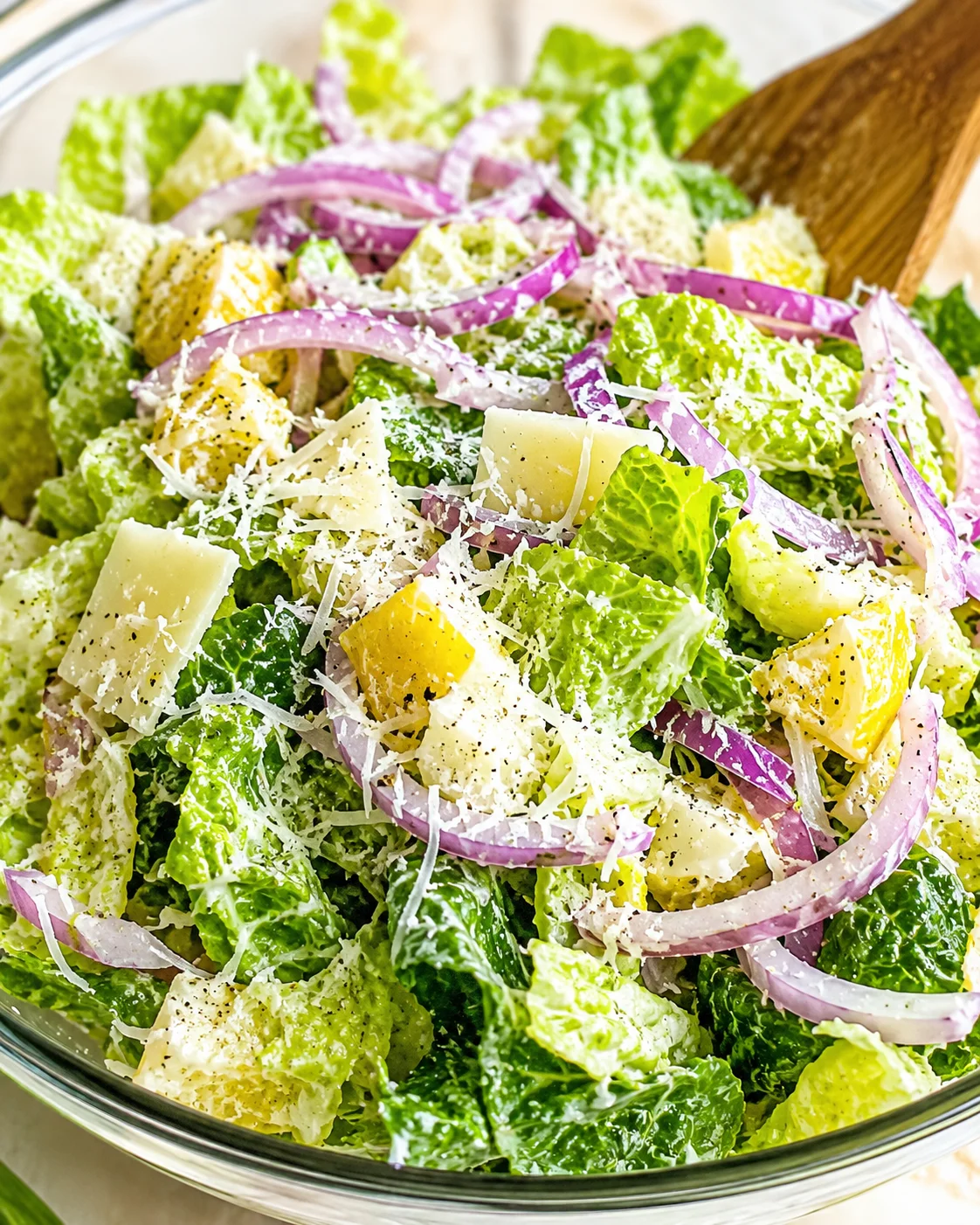 Bright bowl of romaine lettuce salad with red onion slices, shaved Parmesan, and yellow cheese chunks.