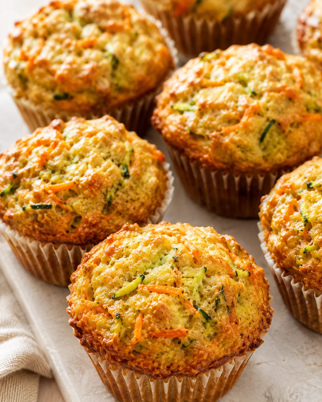 Golden-brown savory muffins with shredded carrot and zucchini in paper liners on a baking sheet