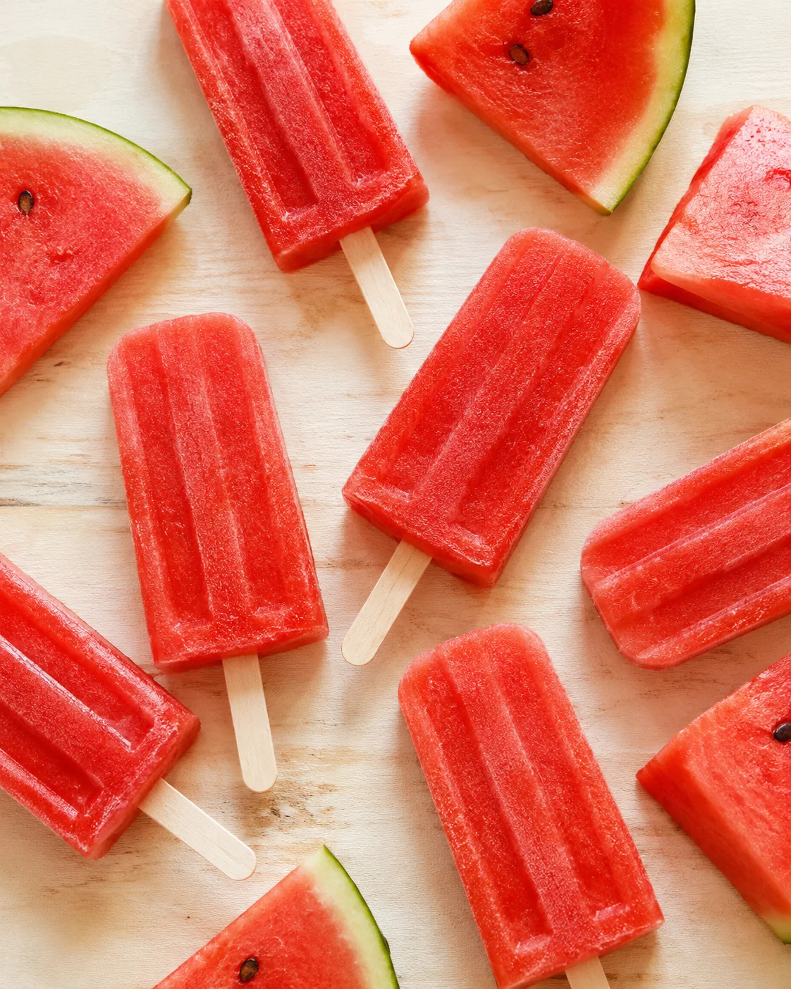 Bright red watermelon popsicles on a wooden surface with watermelon slices.