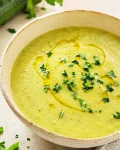 A bowl of creamy zucchini soup garnished with herbs and olive oil.