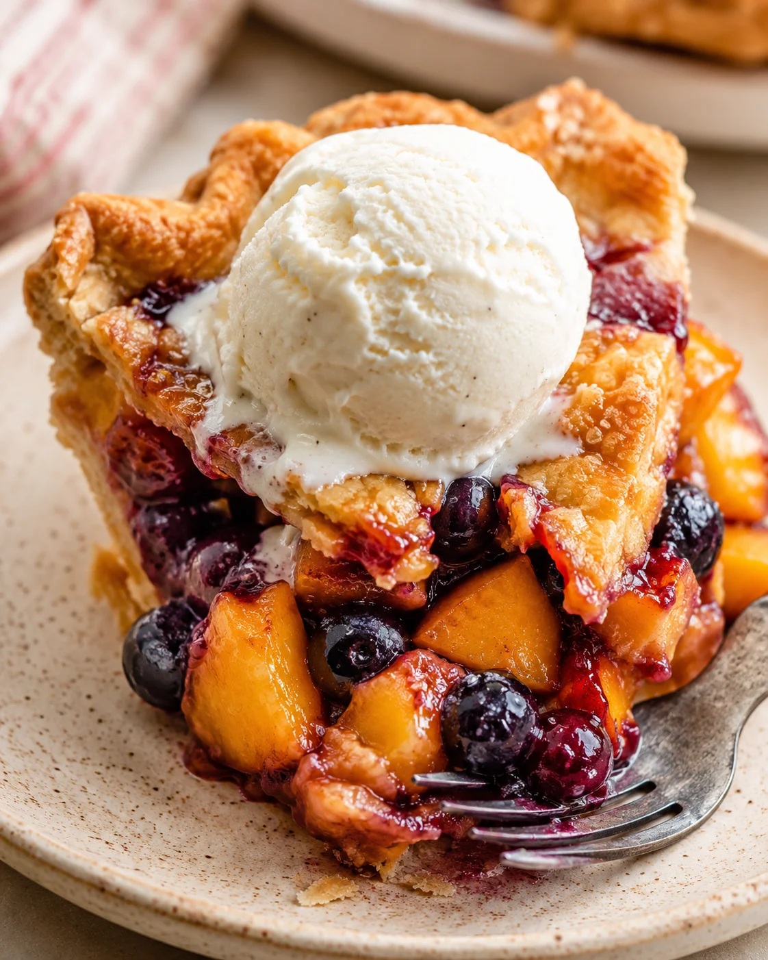 Close-up of blueberry peach pie topped with vanilla ice cream on a plate.