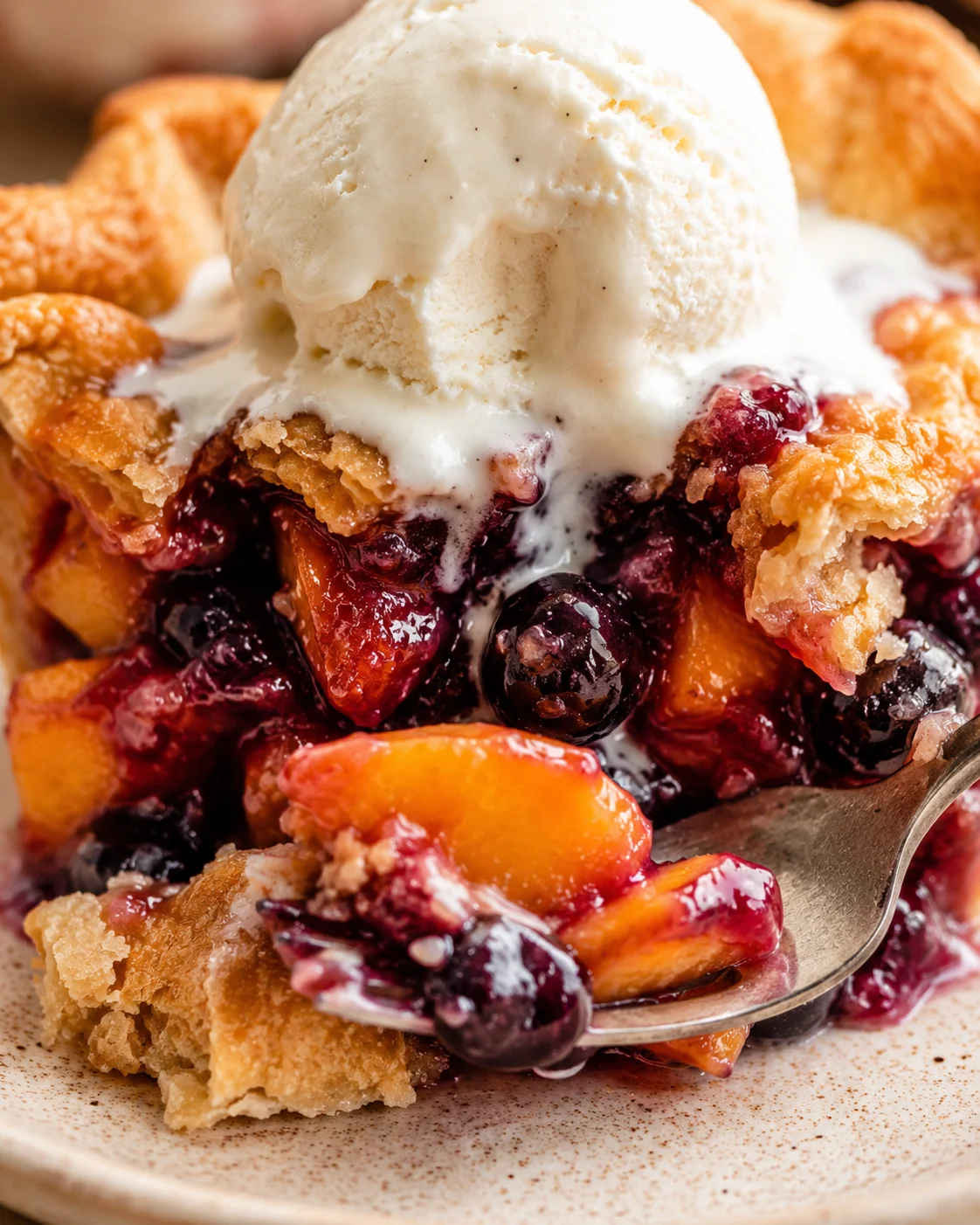 Close-up view of a freshly baked blueberry peach pie with a scoop of vanilla ice cream on top.