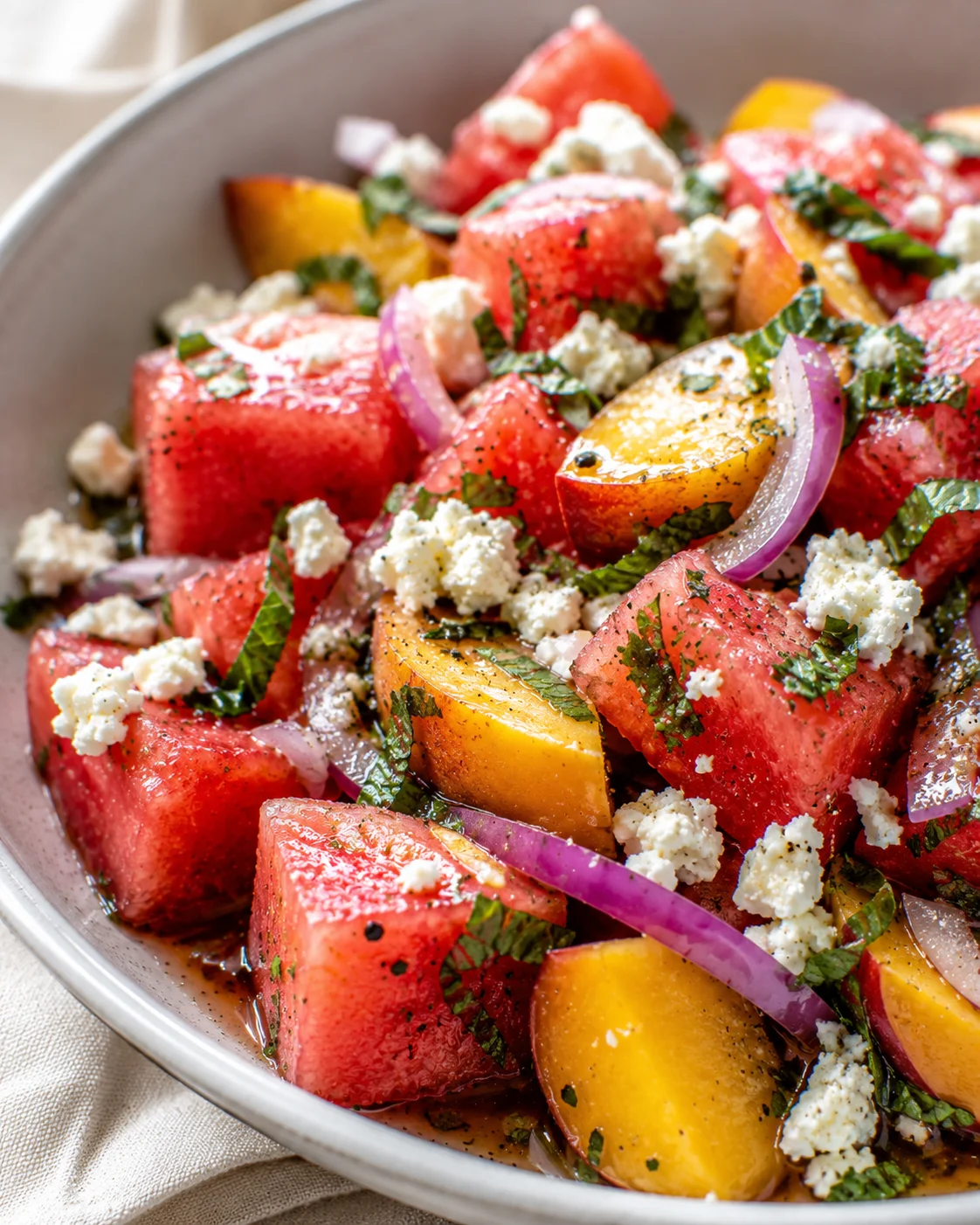 Juicy watermelon and sweet peaches mixed with feta and herbs in a vibrant salad.