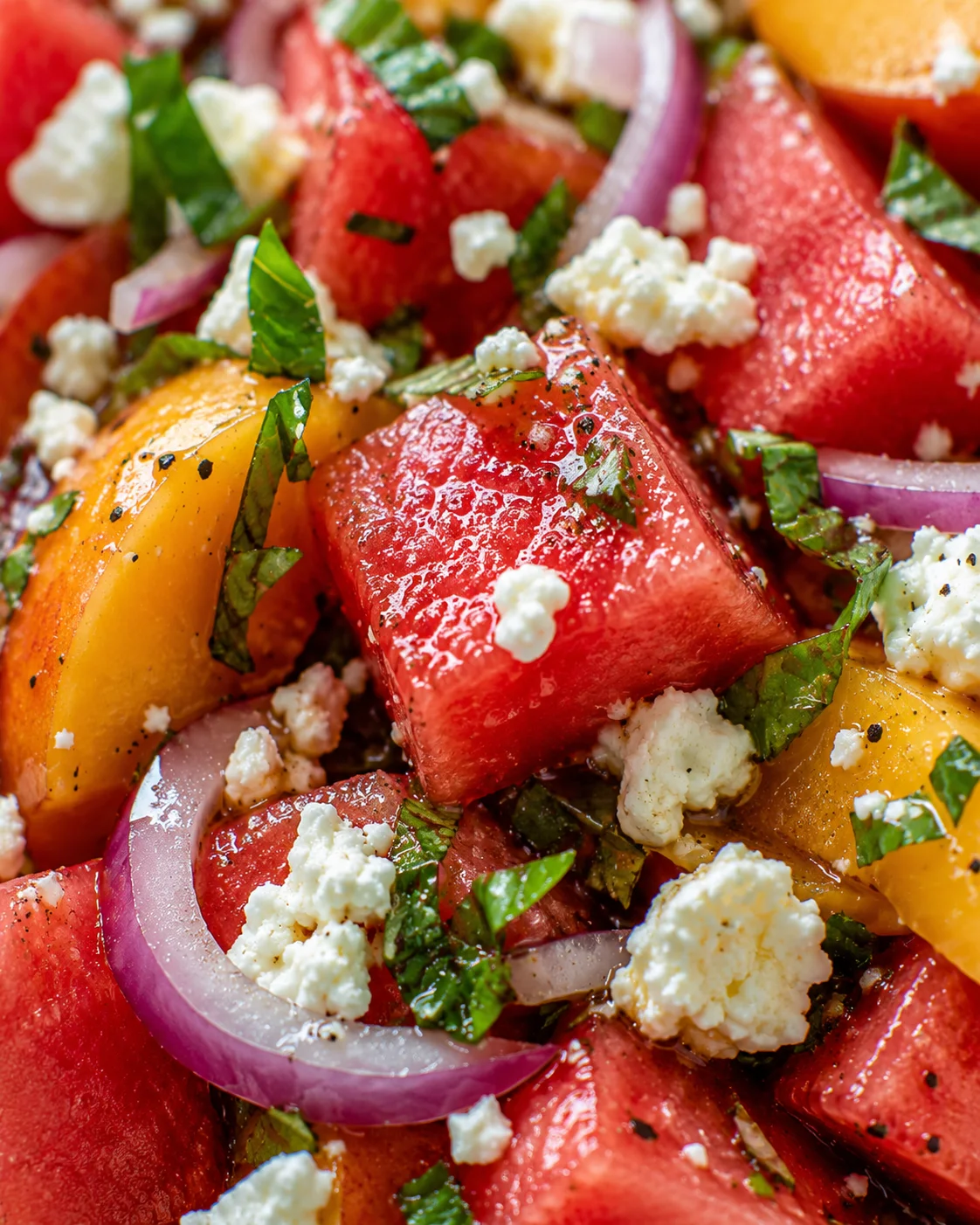 Close-up of a vibrant watermelon, peach, and feta salad with herbs and dressing