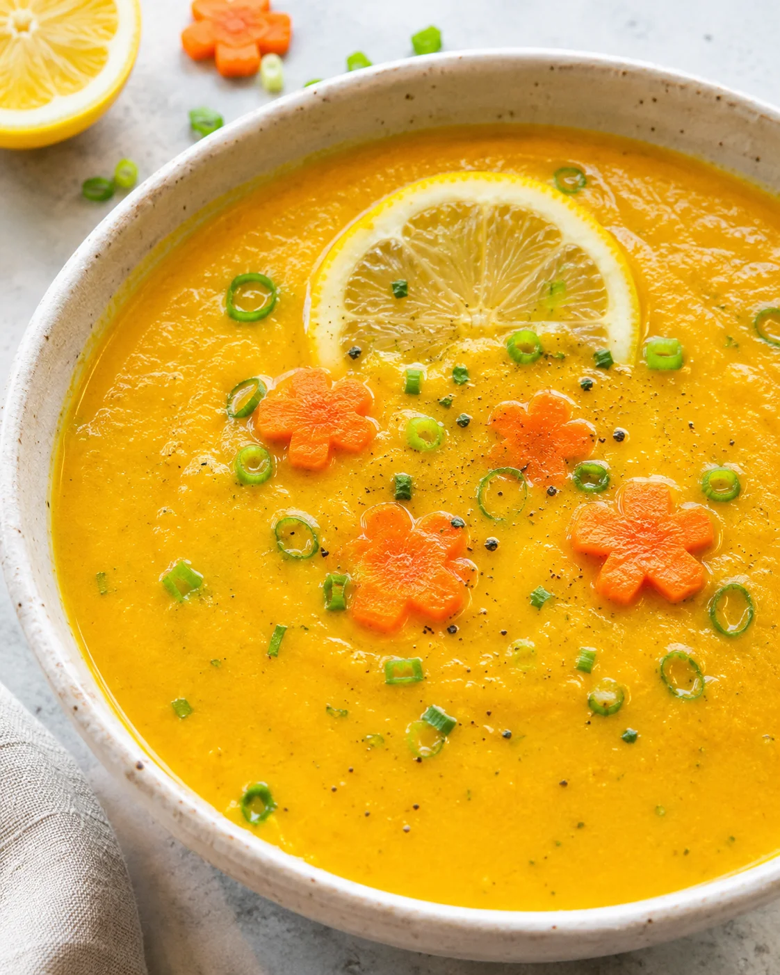 Creamy, vibrant carrot zucchini soup garnished with lemon slices and herbs