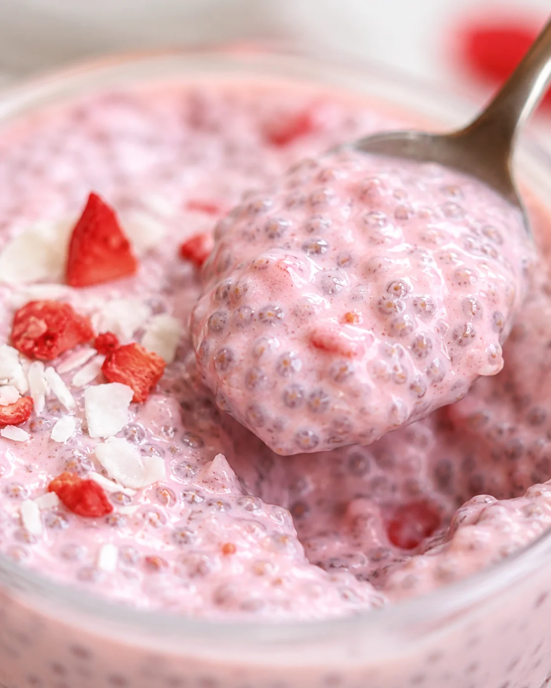 Creamy Strawberry Chia Pudding Close-up of pink strawberry chia pudding with toppings and a spoon in a glass.